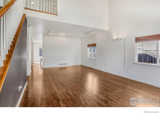 unfurnished living room with visible vents, rail lighting, baseboards, and wood finished floors