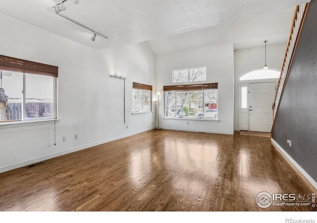 unfurnished living room featuring track lighting, visible vents, wood finished floors, baseboards, and high vaulted ceiling