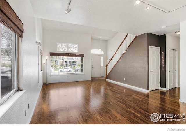 unfurnished living room with plenty of natural light, rail lighting, and wood finished floors