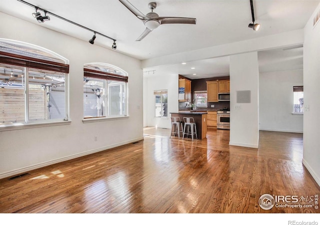 living room with a ceiling fan, visible vents, rail lighting, wood finished floors, and baseboards