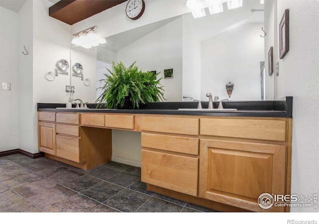 bathroom with double vanity, baseboards, a sink, and stone tile flooring