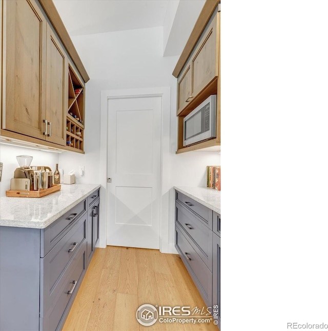 2890 Curtis St, Denver, CO 80205 - kitchen with stainless steel microwave, light wood-style flooring, gray cabinets, and light stone countertops