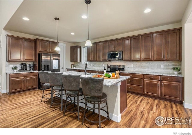 kitchen featuring a kitchen island with sink, a breakfast bar area, tasteful backsplash, light wood-style flooring, and stainless steel appliances