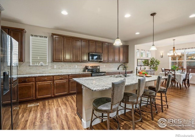 kitchen featuring decorative backsplash, appliances with stainless steel finishes, a sink, light wood finished floors, and a breakfast bar