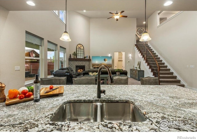 kitchen with ceiling fan, a high ceiling, a sink, stone countertops, and a tile fireplace