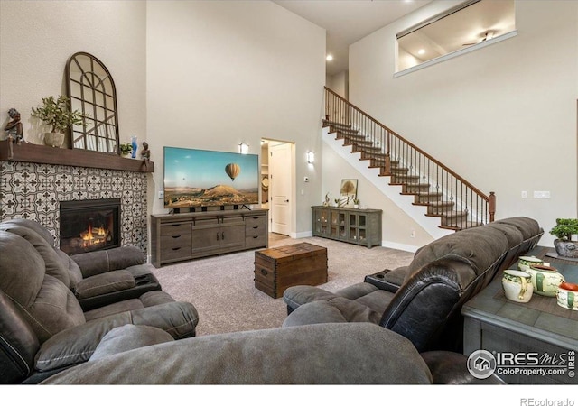 carpeted living area with stairs, baseboards, a tiled fireplace, and a towering ceiling