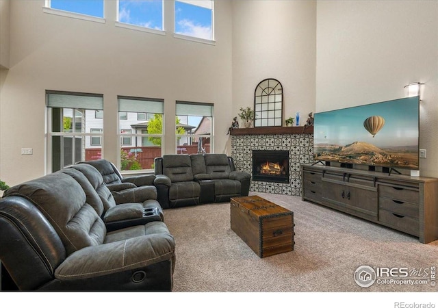 carpeted living area featuring a stone fireplace, a high ceiling, and a healthy amount of sunlight