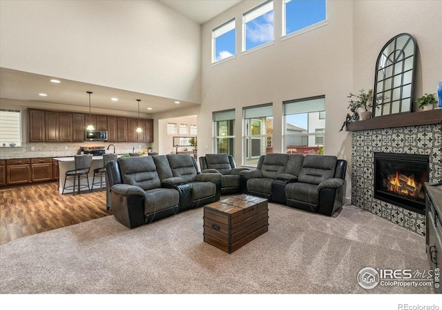 carpeted living room with recessed lighting, a high ceiling, a fireplace, and wood finished floors