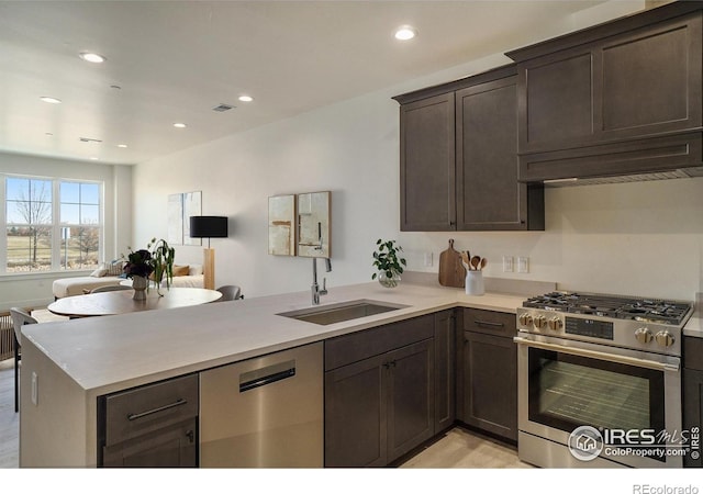 kitchen featuring appliances with stainless steel finishes, a sink, a peninsula, open floor plan, and dark brown cabinetry