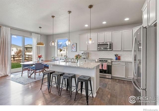 4408 Fox Grove Dr, Fort Collins, CO 80524 - kitchen featuring appliances with stainless steel finishes, dark wood-style floors, a kitchen island with sink, a kitchen breakfast bar, and decorative backsplash