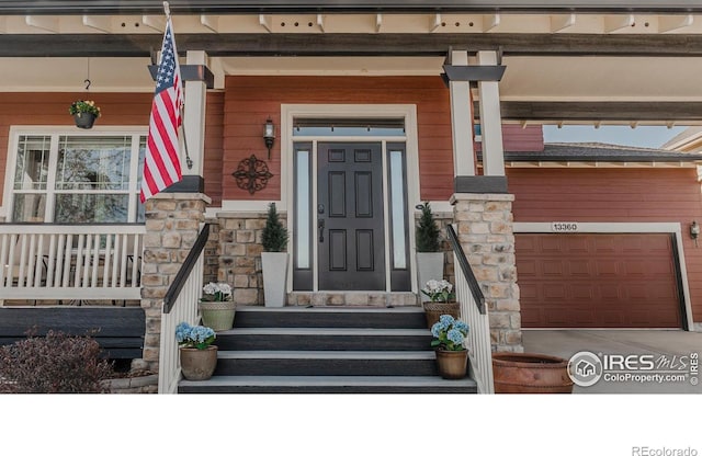 doorway to property featuring a garage, covered porch, and stone siding