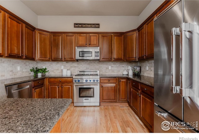 kitchen with decorative backsplash, brown cabinets, light wood-type flooring, dark stone counters, and stainless steel appliances