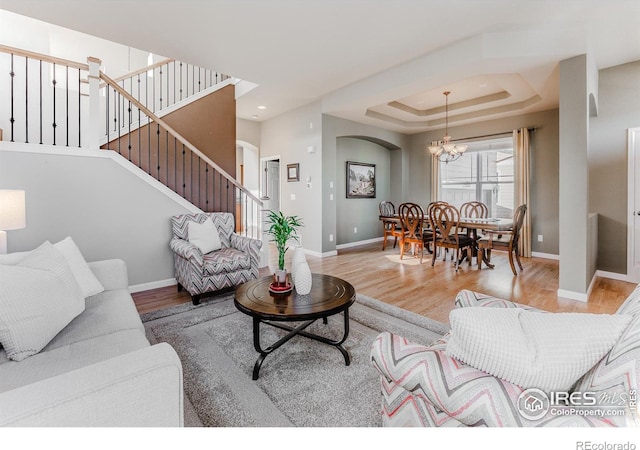 living area with wood finished floors, stairway, baseboards, a raised ceiling, and an inviting chandelier