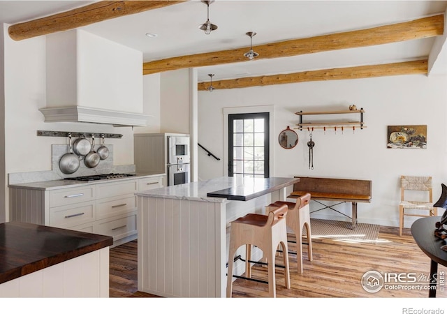 15789 N 83rd St, Longmont, CO 80503 - kitchen with beamed ceiling, appliances with stainless steel finishes, light wood-style flooring, white cabinets, and a kitchen bar