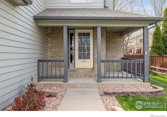 2476 Forsythia Dr, Loveland, CO 80537 - view of exterior entry with a porch, roof with shingles, fence, and brick siding
