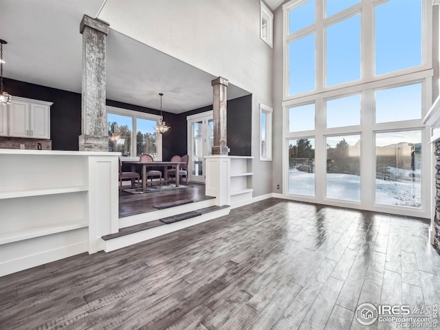 unfurnished living room featuring dark wood-style flooring, ornate columns, baseboards, and an inviting chandelier