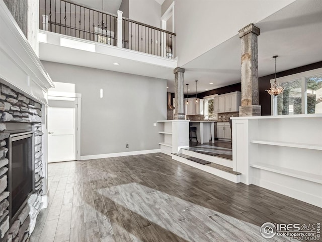 unfurnished living room featuring a high ceiling, a chandelier, a stone fireplace, and wood finished floors