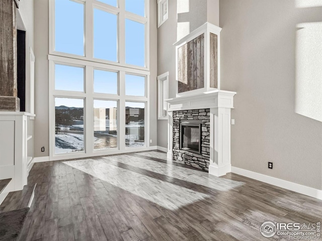 unfurnished living room with dark wood-style flooring, a high ceiling, a stone fireplace, and baseboards