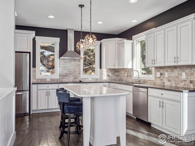 kitchen with a kitchen island, dark wood-style flooring, white cabinetry, stainless steel appliances, and wall chimney exhaust hood