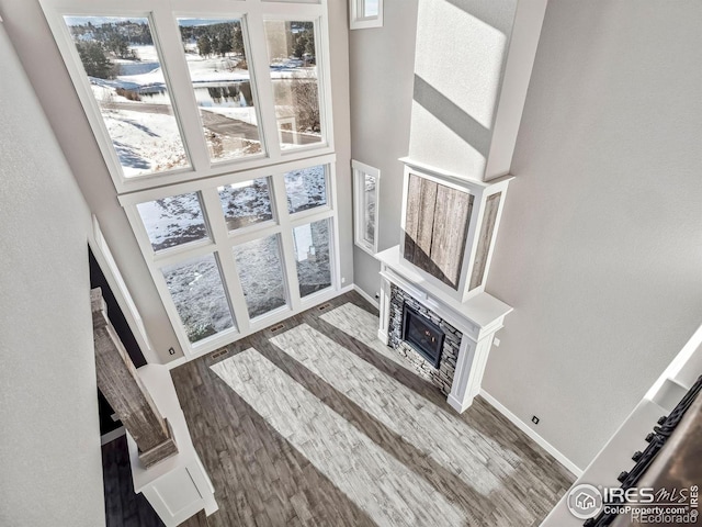 unfurnished living room with baseboards, a glass covered fireplace, wood finished floors, and a towering ceiling
