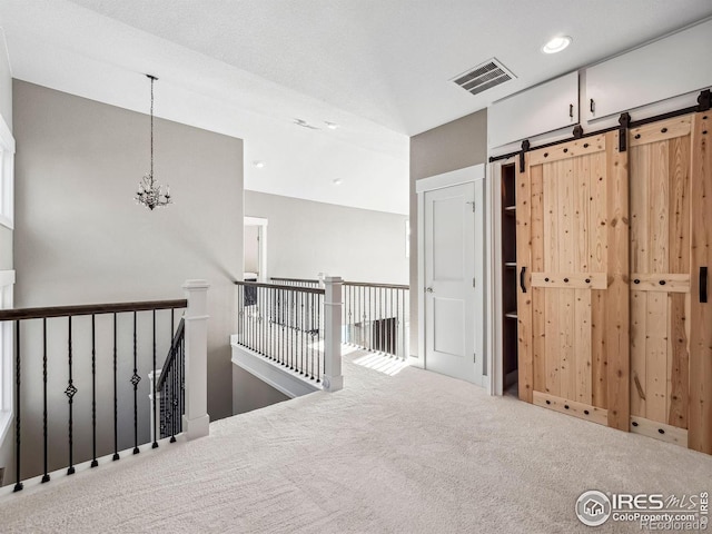 interior space with visible vents, a barn door, carpet flooring, a notable chandelier, and an upstairs landing