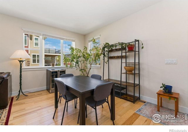 dining room featuring baseboards, wine cooler, and light wood-style floors