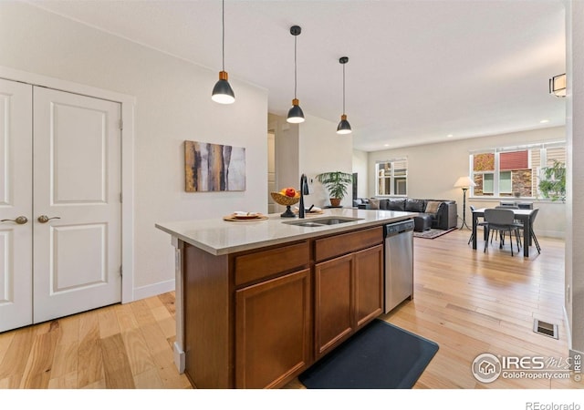 kitchen with visible vents, brown cabinetry, stainless steel dishwasher, a sink, and light wood finished floors