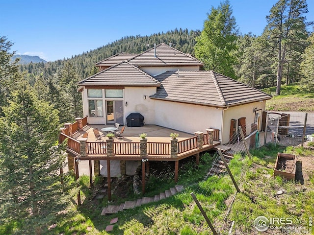 27921 Alabraska Ln, Evergreen, CO 80439 - back of property featuring a wooded view, stucco siding, a wooden deck, a tiled roof, and a vegetable garden