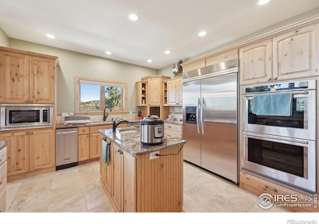 27921 Alabraska Ln, Evergreen, CO 80439 - kitchen with built in appliances, light brown cabinetry, a center island with sink, recessed lighting, and light stone countertops