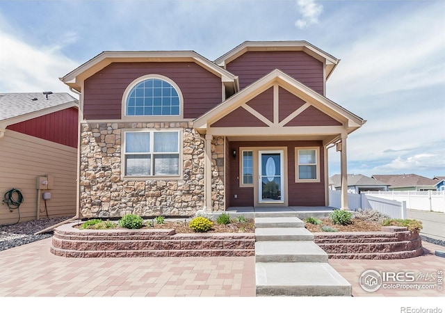 craftsman-style home with fence, a porch, and stone siding