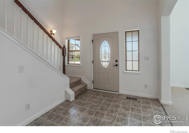 foyer entrance with baseboards, a high ceiling, visible vents, and stairway