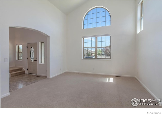 carpeted entrance foyer with arched walkways, baseboards, a wealth of natural light, and a towering ceiling
