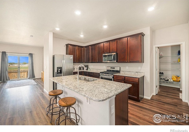 kitchen featuring a kitchen breakfast bar, a center island with sink, a sink, dark wood-style floors, and stainless steel appliances