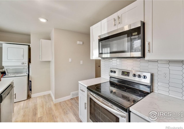 221 Chestnut St, Windsor, CO 80550 - kitchen with appliances with stainless steel finishes, stacked washing machine and dryer, white cabinetry, light wood-style floors, and backsplash