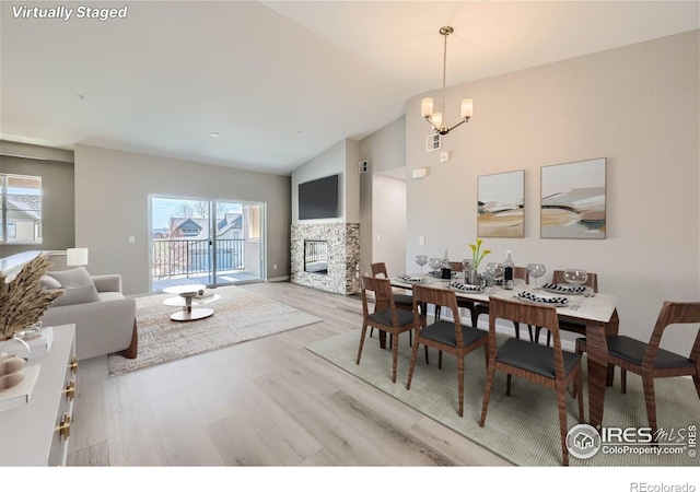 dining room featuring an inviting chandelier, a healthy amount of sunlight, wood finished floors, and a fireplace