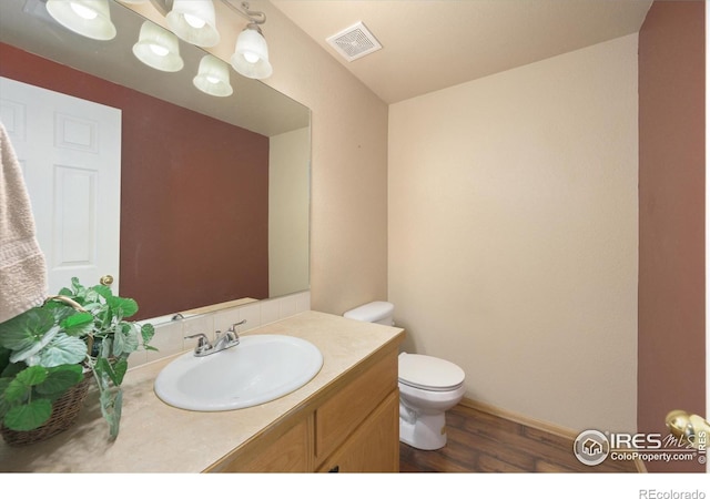 bathroom featuring visible vents, wood finished floors, vanity, baseboards, and toilet