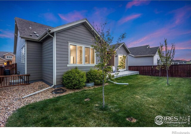719 Wagon Bend Rd, Berthoud, CO 80513 - back of property at dusk featuring fence, a lawn, and roof with shingles
