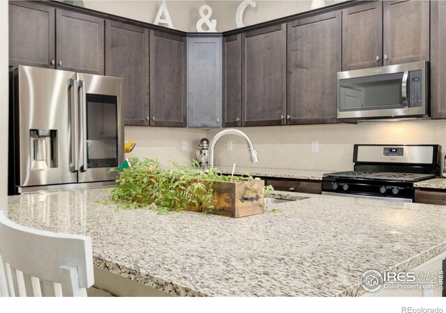 719 Wagon Bend Rd, Berthoud, CO 80513 - kitchen with stainless steel appliances, dark brown cabinetry, light stone countertops, and tasteful backsplash