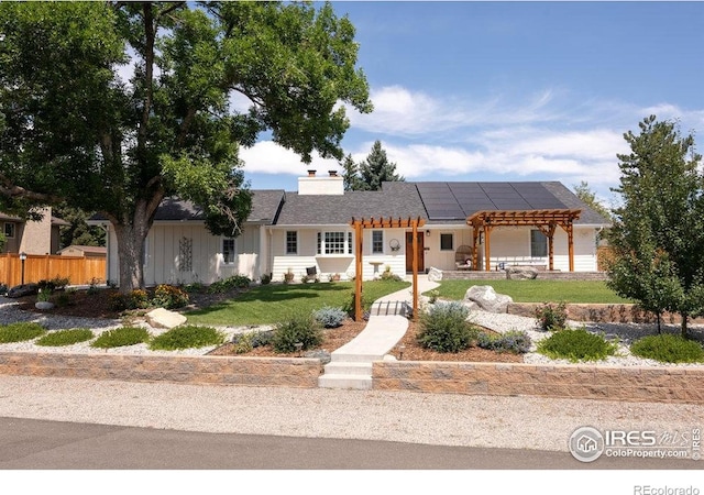 ranch-style house featuring a front lawn, fence, a pergola, board and batten siding, and roof mounted solar panels