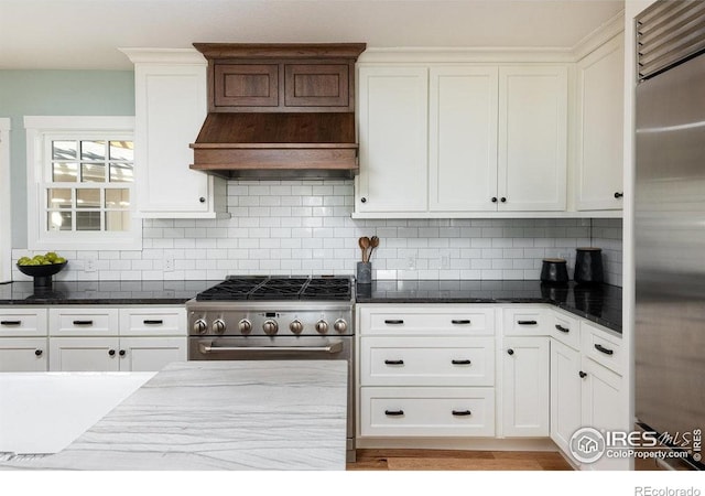 kitchen with white cabinetry, backsplash, high quality appliances, and dark stone counters