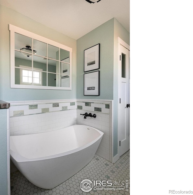full bath with a soaking tub, tile walls, tile patterned flooring, and a wainscoted wall