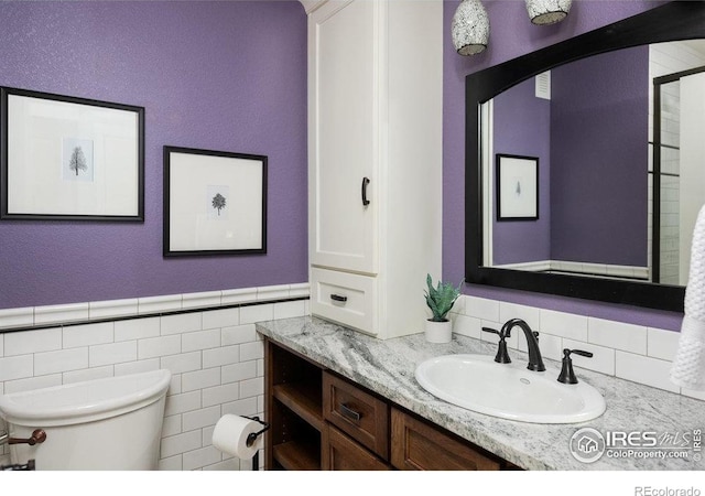 bathroom with vanity, wainscoting, toilet, and tile walls