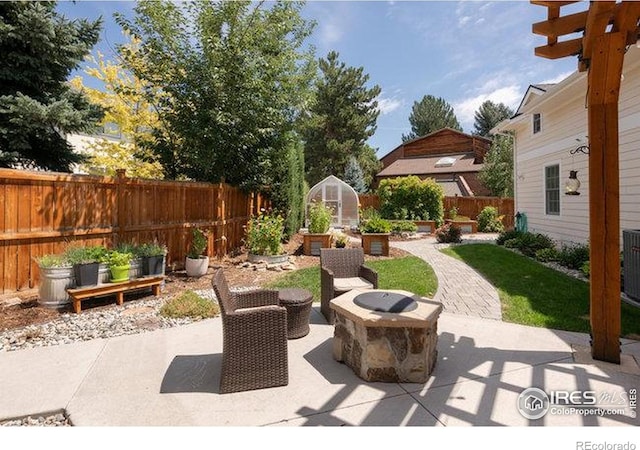 view of patio / terrace with a fire pit, a greenhouse, an outdoor structure, a fenced backyard, and a vegetable garden