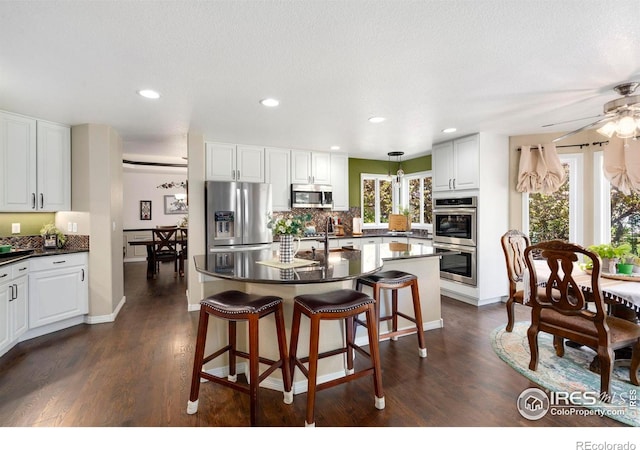 5442 Tiller Ct, Windsor, CO 80528 - kitchen featuring dark wood-type flooring, appliances with stainless steel finishes, dark countertops, and a kitchen breakfast bar