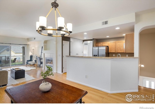 dining space with a chandelier, light wood-type flooring, arched walkways, recessed lighting, and a tiled fireplace