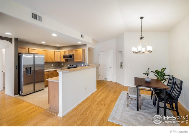 kitchen with appliances with stainless steel finishes, arched walkways, light wood-style floors, light countertops, and recessed lighting
