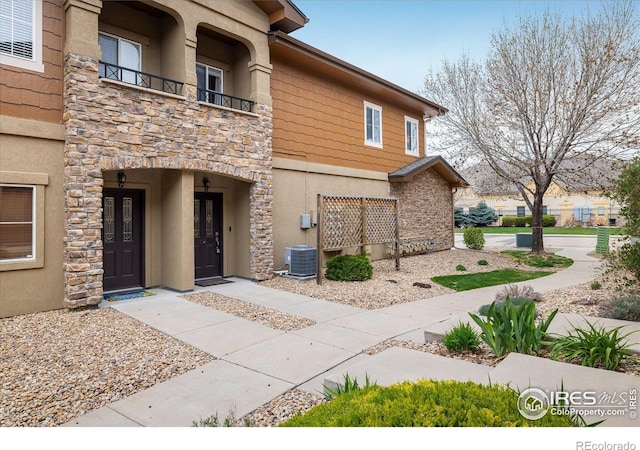 exterior space featuring stone siding, stucco siding, a balcony, and central AC