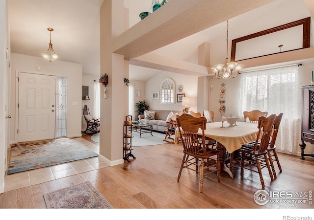 dining area with baseboards, light wood-style flooring, a chandelier, and high vaulted ceiling