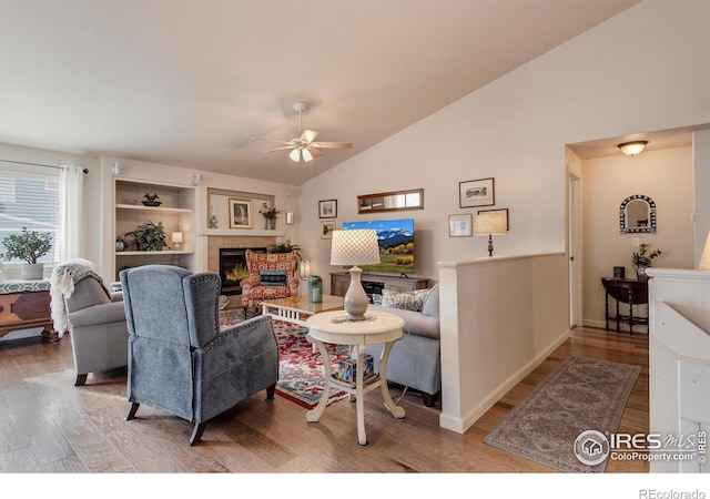 living room with a glass covered fireplace, ceiling fan, vaulted ceiling, and wood finished floors