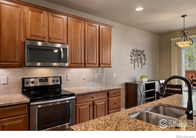 850 Prairiestar Dr, Berthoud, CO 80513 - kitchen featuring brown cabinets, appliances with stainless steel finishes, a sink, decorative light fixtures, and backsplash
